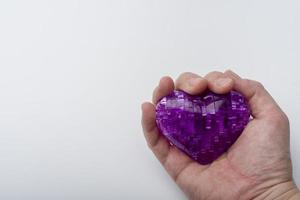 The hand holds the heart on a white plastic background. photo