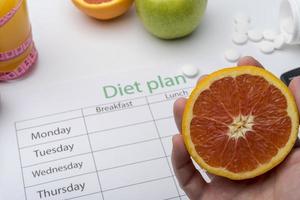 The hand holding the grapefruit over a diet plan. photo