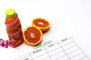 plan de dieta y botella de jugo de toronja con toronja fresca sobre fondo blanco. foto