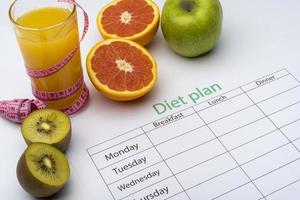 Diet plan on a piece of paper, next to a glass of orange juice. Fresh grapefruit, kiwi and Apple with centimeter on white background. photo