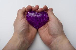 The hand holds the heart on a white plastic background. photo