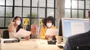 två kvinnliga arbetskamrater team med ansiktsmask som arbetar i nya normala kontor. covid-19-skydd genom frigjord partition, kontor på arbetsplatsen, social distansering för pandemihälsa, förebyggande av sjukdomar. video