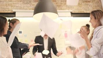 L'équipe de jeunes collègues multiraciaux du bonheur célèbre le succès commercial avec un patron caucasien en jetant des papiers et en applaudissant, joyeuse lorsque la réunion se termine dans le lieu de travail d'un bureau. video