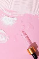 Dropper and smears of cream, ubtan and oil on pink surface - cosmetics and spa care products top view photo