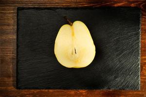 Half natural yellow pear on a slate board, close-up, on a wooden table, top view photo