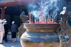 varitas de incienso ardiendo en una olla grande como ofrenda del templo. Vietnam. personas incidentales en el fondo foto