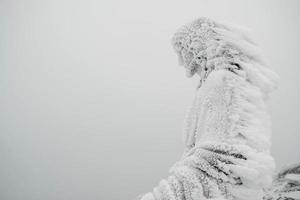 The statue of Jesus is covered with snow and ice on top of the mountain photo