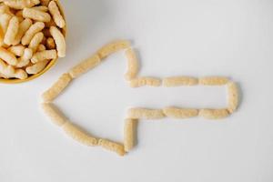 Corn sticks in a yellow bowl scattered in the shape of an pointer on a white background. Top view. Place for your text photo