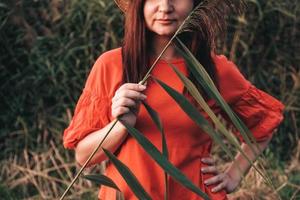 retrato de una mujer hermosa con un sombrero de paja y vestida con ropa roja sobre un fondo de juncos foto