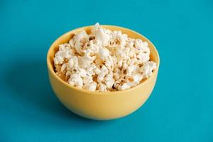 Popcorn in a yellow bowl on a blue background. Copy, empty space for text photo