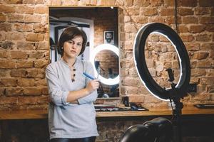 Young beautiful hairdresser woman with razor in hand against a brick wall background. Barbershop advertising concept. Place for text or advertising photo