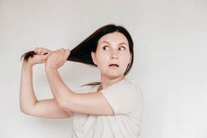Shocked panic brunette woman dressed in casual white t shirt pulls her hands by her hair and screaming in despair and frustration, her eyes full of terror, mouth open. Copy, empty space for text photo
