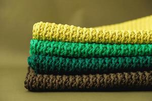 Stack of knitted material from threads of yellow, green, brown colors on a green background. Copy, empty space for text photo