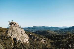 Landscape with high stone rock in a green forest under a blue sky on a background of mountains. Copy, empty space for text photo