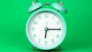 el despertador azul muestra el paso del tiempo. el movimiento de las manecillas del reloj pasó rápidamente. en el fondo verde.