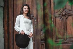 Woman wearing in white clothes, holding knitted bag on the background of old wooden doors photo