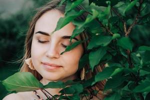 retrato de una hermosa chica rubia con los ojos cerrados en un árbol de hojas verdes. copiar, espacio vacío para texto. copiar, espacio vacío para texto foto