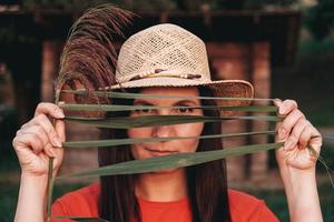 Portrait of a beautiful woman in a straw hat looking into camera through the reed leaves photo