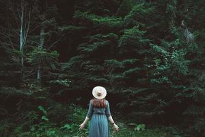 Woman in a straw hat and dress stands on a background of green forest and trees photo