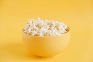 Popcorn in a yellow bowl on a yellow background. Copy, empty space for text photo
