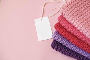 Stack of knitted material from threads of pink, red, purple colors with blank Price Tag on a pink background. Top view. Copy, empty space for text photo