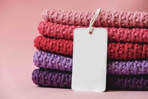 Stack of knitted material from threads of pink, red, purple colors with blank Price Tag on a pink background. Copy, empty space for text photo