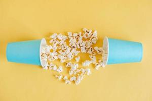 palomitas de maíz en vasos de papel azul esparcidos sobre un fondo amarillo. vista superior. copiar, espacio vacío para texto foto