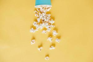 Popcorn in a blue paper cup scattered on a yellow background. Minimalist concept. Top view. Copy, empty space for text photo