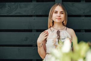 Portrait of a beautiful blonde woman dressed in flower dress in a green leaves trees on a wooden wall background. Copy, empty space for text photo