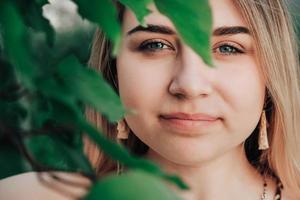 Portrait of a beautiful blonde girl with natural beauty in a green leaves trees. Copy, empty space for text photo