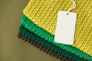 Stack of knitted material from threads of yellow, green, brown colors with blank Price Tag on a green background photo