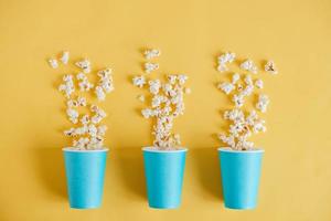 Popcorn in blue paper cups scattered on a yellow background. Top view. Copy, empty space for text photo