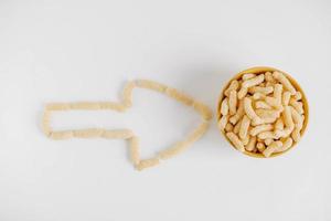 Corn sticks in a yellow bowl scattered in the shape of an pointer on a white background. Top view. Place for your text photo