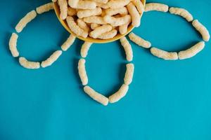Corn sticks in a bowl in the shape of a flower on a blue background. Top view. Place for your text photo