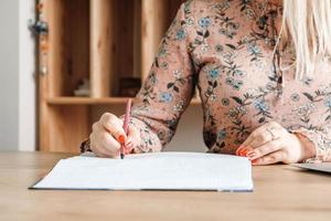 Woman hands with pencil, she is is writing in her notebook sitting at the table with book shelf background. Copy, empty space for text photo
