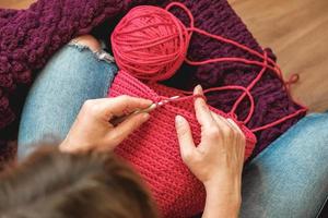 Hands woman in a cozy home setting knits from a pink thread. Top view. Copy, empty space for text photo