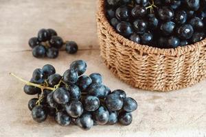 Bunch of black grapes in a round wicker basket on a old wooden table. Copy, empty space for text photo