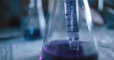 vetenskapsman tar ut en lila vätska från en konisk kolv i ett labb video