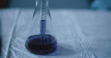 Scientist taking out a purple liquid from a conical flask in a lab, slow motion video