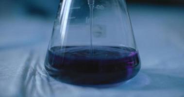 Wissenschaftler, der eine violette Flüssigkeit in einen Kolben gibt, um Chemikalien in einem Labor zu testen.