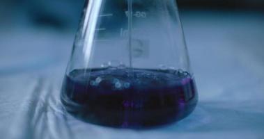 científico que agrega un líquido púrpura a un matraz para probar productos químicos en un laboratorio.