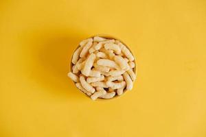 Corn sticks in a yellow bowl on a yellow background. Top view. Place for your text photo