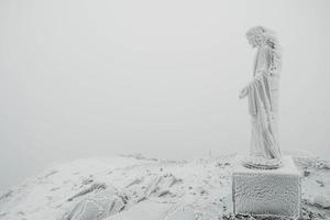 The statue of Jesus is covered with snow and ice on top of mountain photo