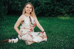 Beautiful blonde woman dressed in flower dress sitting on the green grass lawn. Copy, empty space for text photo