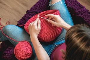 Hands woman in a cozy home setting knits from a pink thread. Top view. Copy, empty space for text photo