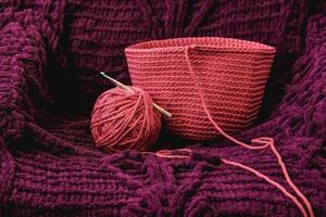 Ball of pink thread with a needle and knitted fabric on a background of purple material. Copy, empty space for text photo