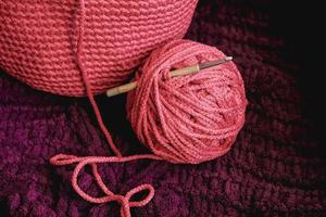 Ball of pink thread with a needle and knitted fabric on a background of purple material. Copy, empty space for text photo