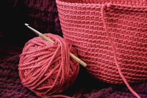 Ball of pink thread with a needle and knitted fabric on a background of purple material. Copy, empty space for text photo