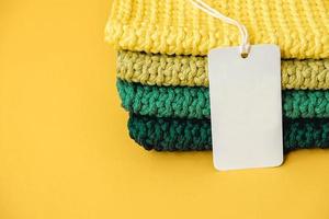 Stack of knitted material from threads of yellow, green, brown colors with blank Price Tag on a yellow background. Copy, empty space for text photo