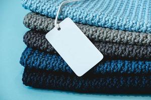 Stack of knitted material from threads of dark blue, light blue, gray colors with blank Price Tag on a blue background. Copy, empty space for text photo